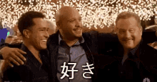 three men are posing for a picture together in front of a crowd with chinese writing .