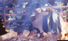 a man and a woman are laying in a pile of hay behind a wooden fence .