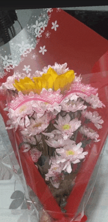a bouquet of pink and yellow flowers wrapped in a red wrapper