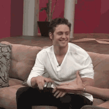 a man in a white shirt is sitting on a couch talking to another man