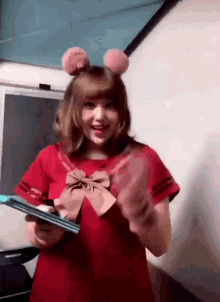 a girl wearing a red dress and pink ears is holding a book