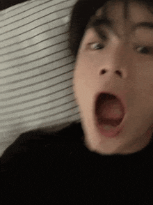 a man is making a funny face while laying on a bed with his mouth open .
