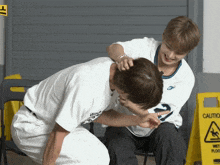 two men are playing with each other in front of a caution sign
