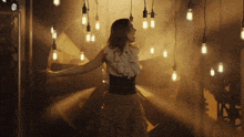 a woman in a ruffled top is standing in a dark room with lots of light bulbs hanging from the ceiling