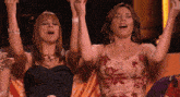 two women are sitting on a couch with their hands in the air