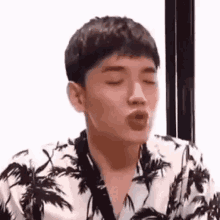 a man is blowing a kiss while wearing a palm tree shirt .