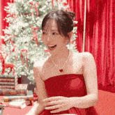 a woman in a red dress is smiling in front of a christmas tree .