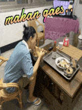 a man is sitting at a table eating food with the words makan gaes written above him