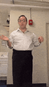a man in a white shirt and black pants stands in front of a fire alarm