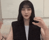a woman with long black hair and bangs is wearing a black vest and a white t-shirt .
