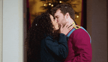 a man and a woman kiss in front of a christmas tree