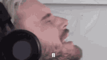 a man with a beard is wearing headphones and making a funny face with his mouth open .