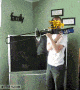 a man playing a trombone in front of a tv with a family sign on the wall