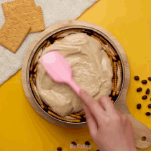 a person is using a pink spatula to spread a creamy sauce on top of a pie