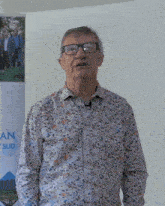 a man wearing glasses and a floral shirt is standing in front of a sign that says " an "