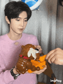 a man in a pink sweater is holding a toy bulldog that says imgplay on it