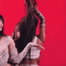 a group of women are standing next to each other on a red background and one of them is holding another woman 's hair .