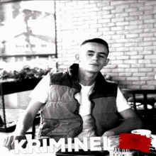 a man in a vest sits at a table in front of a brick wall with the word kriminal on the bottom