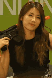 a woman is holding a gun in front of a green sign that says nin