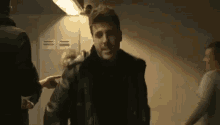a man in a black jacket is standing in a dark room with a woman pointing at him .