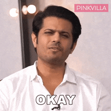 a man in a white shirt is making a funny face and the word okay is on the shirt