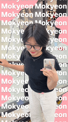 a woman wearing glasses and a black shirt is holding a cell phone in front of a collage of words including mokyeon