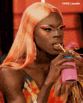a drag queen with orange hair is drinking through a straw