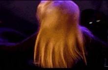 a woman with long blonde hair is standing in a dark room with purple lights behind her .