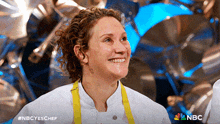 a woman in a chef 's uniform is smiling with the nbc logo behind her