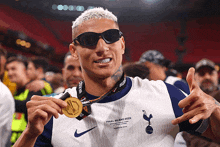 a man wearing sunglasses holds up a medal that says final uefa league 2020