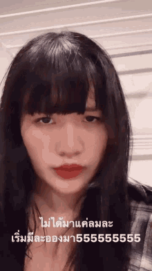 a woman with long black hair and bangs is wearing red lipstick and a plaid shirt