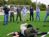 a group of men are standing on a soccer field watching a man laying on the ground