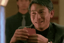 a man in a suit is smiling while holding a playing card in his hand .