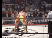 two women are wrestling in a ring with a referee in the background .