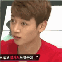a young man in a red shirt is looking at the camera with a sign in the background that says ' ? '
