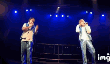 two men singing on a stage with a watermark that says img on it