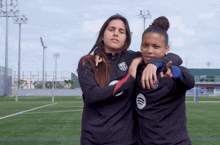 two female athletes are hugging each other on a field and one has a spotify logo on her shirt
