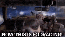 a man is sitting in a car with the words `` now this is podracing '' written on the screen .