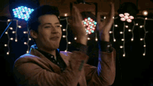 a man in a brown jacket is clapping his hands in front of a bunch of lights