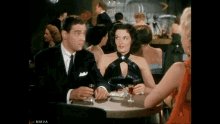 a man and a woman are sitting at a table with a glass of wine .