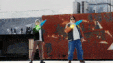 two men standing next to each other holding swords in front of a rusty building