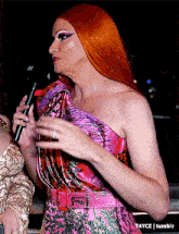 a woman with red hair is holding a microphone in front of a sign that says t4yce