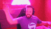 a man wearing headphones and a purple shirt is sitting in a chair with his arms in the air .