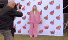 a woman in a pink suit is being photographed by a man in front of a wall that says music tour