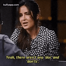 a woman in a black and white polka dot shirt is talking to a man in a room .
