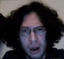 a man with curly hair and glasses is looking at the camera with his mouth open .