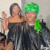 a man with green hair is getting his hair cut by a woman in a black dress