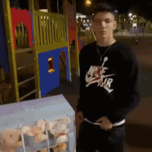 a young man in a nike air sweatshirt is standing in front of a playground .