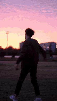 a man is walking in a field at sunset