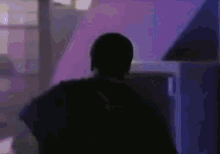 a silhouette of a man in a dark room with purple lights behind him .